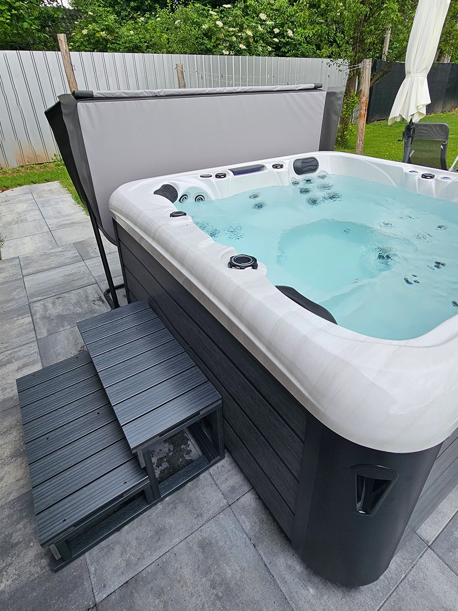 Massage pool Alpha 723 in the garden, next to it there is a stand with a cover and steps.