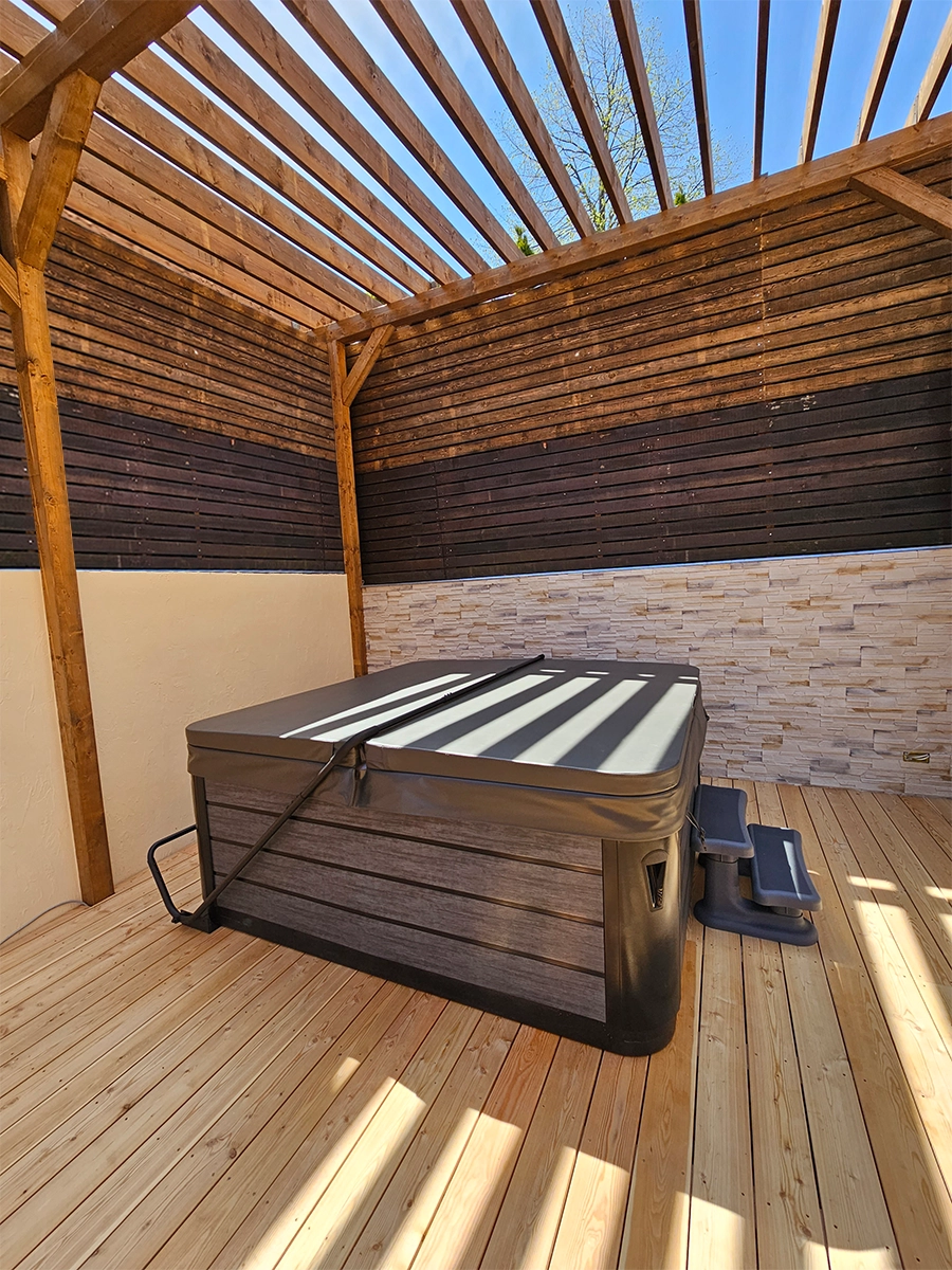 Alpha 723 - hot tub under a wooden pergola on a wooden floor.